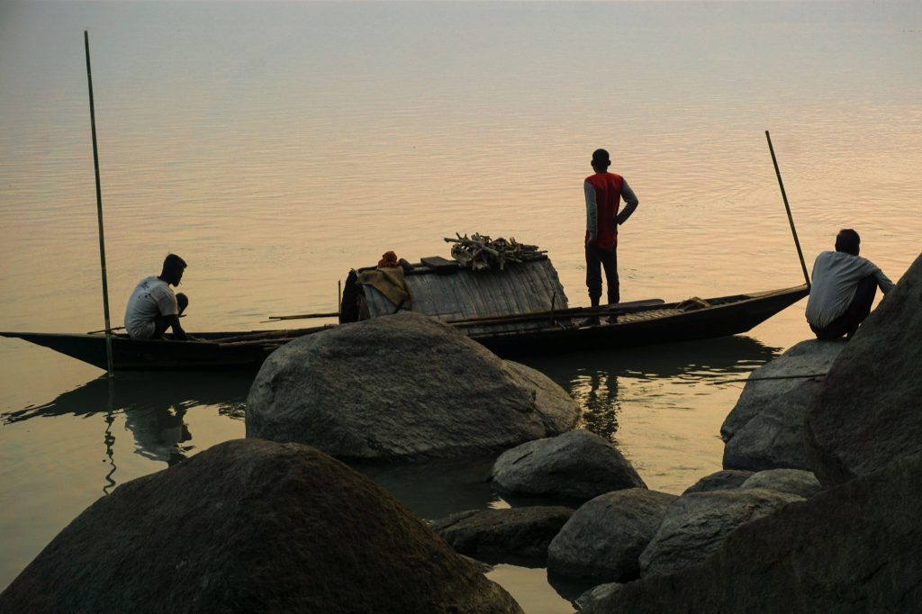 Fishermen returning from the deep waters in the boat. The angler sitting on the rocks was also packing his things up.