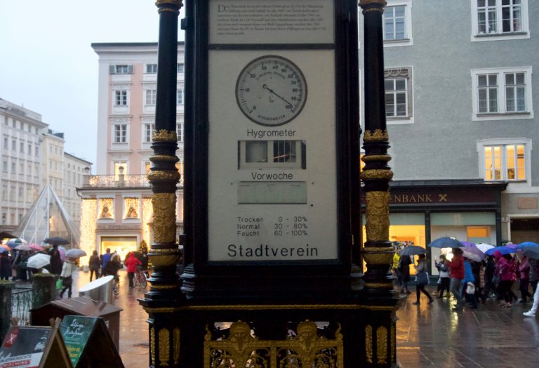 There is a set of analogue meters displaying temperature, pressure and relative humidity right in front of the weather station. It was raining heavily and everyone had taken out their umbrellas.