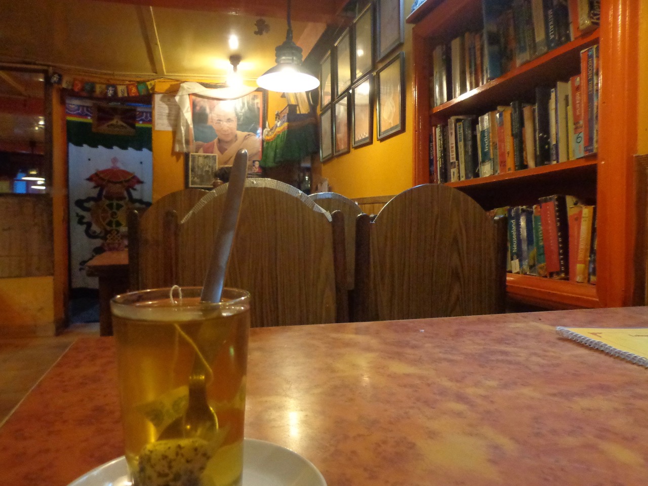 The bookshelf at Lobsang&rsquo;s Four Seasons Cafe overlooking the glass of Tibetan herbal tea.